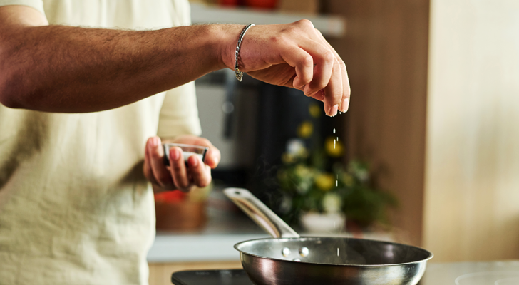 Pessoa temperando com sal a comida dentro de uma panela.
