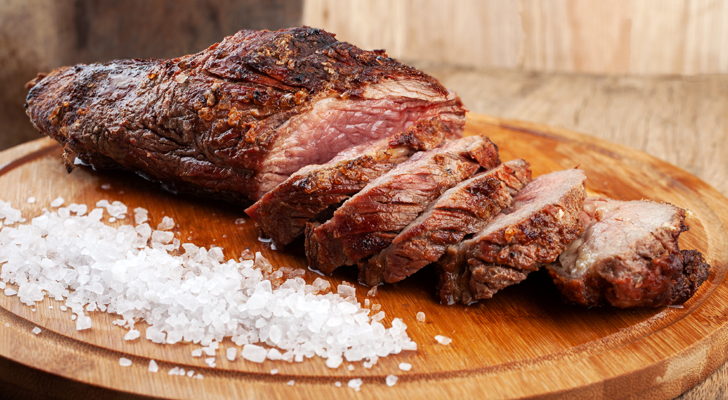 Carne assada fatiada, com sal marinho espalhado na tábua de madeira.